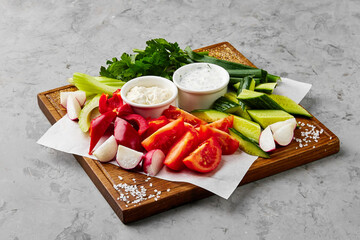 Fresh cut vegetables with sauces and greenery on board