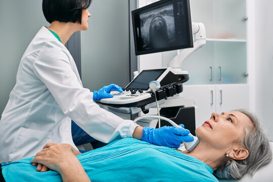 Ultrasound diagnostics of thyroid gland. Endocrinologist making ultrasonography to senior female patient at ultrasound office of medical clinic