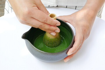 Hand hold whisk preparing and mixing traditional organic Japanese matcha green tea powder with milk...