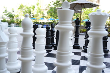 A giant black and white chess set sits on a chessboard. A large plastic chess set is placed in front of the building. For playing games or just for beauty. select focus
