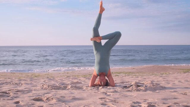 blonde woman doing standing on head yoga asana on the sand beach in front of the sea