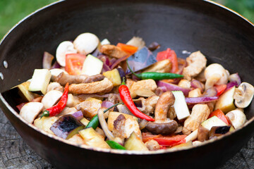spicy fried pork meat with chili peppers and vegetables with mushrooms in a pan