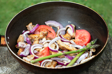 fried pork meat with onions and tomatoes in a frying pan