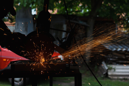 The master cuts the metal with a grinding machine. Sparks from metal in the workshop (shallow DOF)