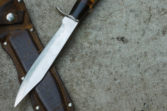 Hunting knife, leather sheath lie on the concrete. Tourist equipment in outdoors. Top view.  Close-up. Copy space