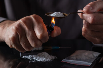 Drug addicts in the dark room. Addict preparing drugs with a spoon and lighter. White powder and a syringe. - obrazy, fototapety, plakaty