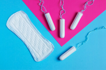 women pads and tampon - sanitary pads lies next to a tampon on an isolated background on a pink and blue background. - obrazy, fototapety, plakaty
