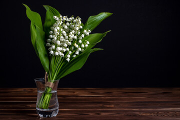 Lily of the valley flowers in glass vase, black background, selective focus
