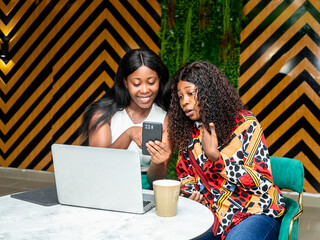 Two women using laptop computer checking their mobile phone in a coffee shop