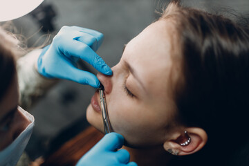 Young woman doing piercing nose ring at beauty studio salon