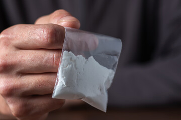 Concept drug addiction. Man hand holds plastic packet or bag with cocaine or another drugs