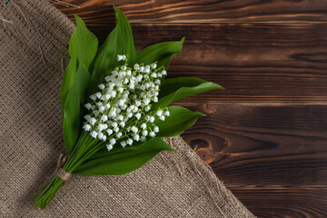 Small and fragrant spring flowers. Bouqet of lily of the valley flowers on dark wooden background