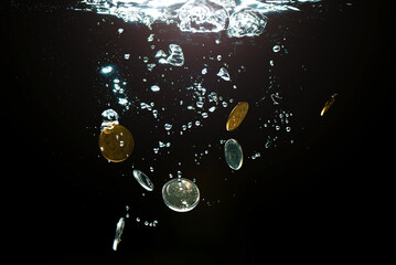 Close-up of money sinking in water. Treasure underwater. Gold and silver coins sink in the sea....