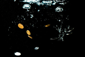 Close-up of money sinking in water. Treasure underwater. Gold and silver coins sink in the sea. Coins under water on a black background.
Sinking money is a sign of a weak economy.