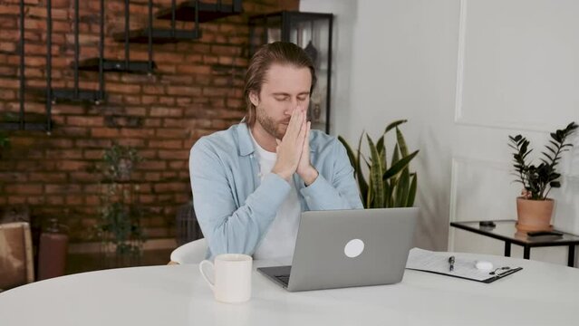 Praying for success. thoughtful young man holding hands on chin and looking at the laptop while sitting at his working place in office