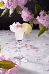 Spring still life with a glass of cold Margarita with lime, pink sakura flowers 