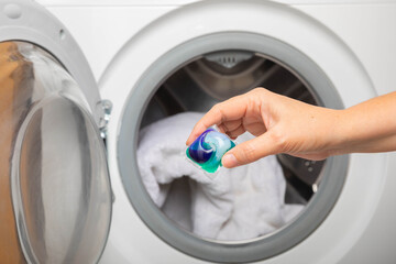 Woman putting laundry detergent capsule into washing machine indoors, closeup.Colorful laundry eco...