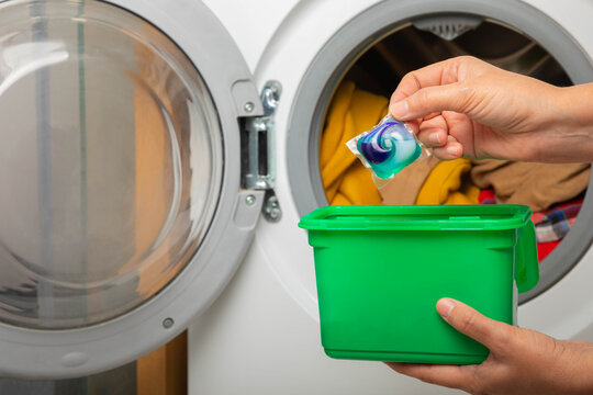 Woman putting laundry detergent capsule into washing machine indoors, closeup.Colorful laundry eco gel in capsule. Washing clothers.The concept of washing and cleanliness