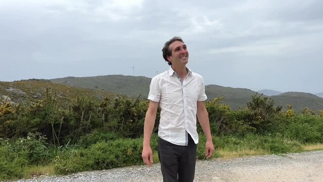 a handsome French or Spaniard man in a white shirt stands against the backdrop of mountains. High quality 4k footage