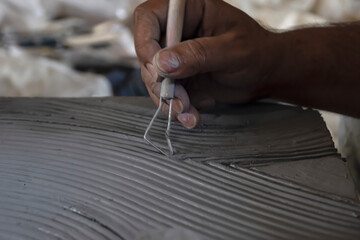 Obraz premium Close up of male sculptor holding tool and making art on clay. Clay master moulding. Clay modelling.