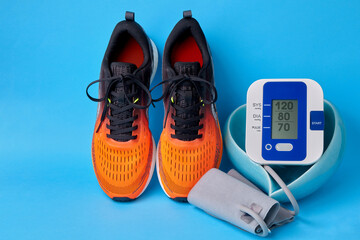 Orange sneakers and blood pressure monitor in a heart-shaped bowl on a blue background