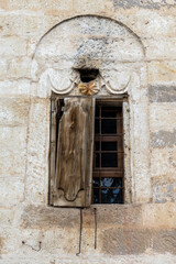 Fototapeta na wymiar Old arched stone window with broken wooden shutters of a greek mansion in Mustafapasa, Cappadocia