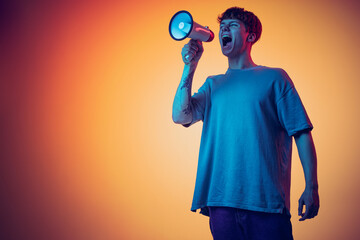 One young red-headed man shouting at megaphone isolated over yellow background in neon. Concept of youth, fashion, emotions, facial expression