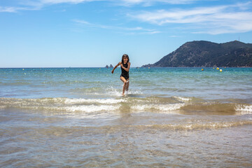 Fototapeta na wymiar Une jolie jeune fille asiatique court heureuse dans l'eau sur la plage
