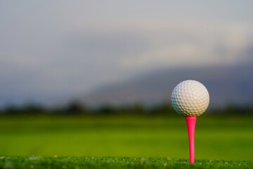 Golf ball on tee in beautiful golf course at sunset background.