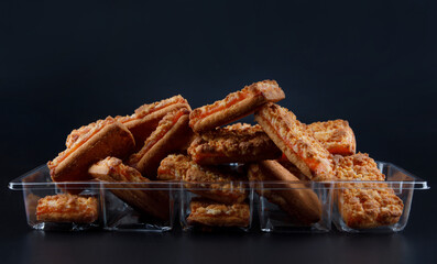 Orange cookies in a plastic container on a dark background .