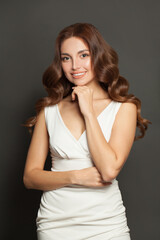 Naklejka premium Cute woman in white dress smiling and standing with crossed arms on gray background.