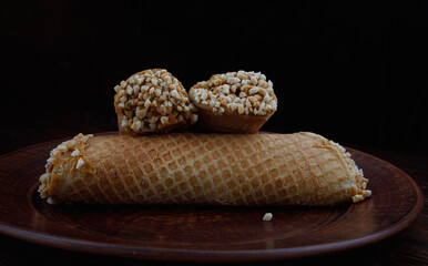 Three waffle tubes with boiled condensed milk and crushed peanuts on a clay plate .