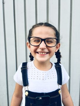 Ni&ntilde;a con gafas, trenza y vestida con un peto vaquero sobre fondo blanco.