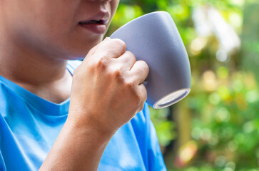 Front view hand of a lady holding a blue ceramic cup of drinks, coffee, and tea in natural background. Enjoy drinking concept.