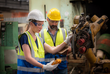 Caucasian female electrical engineer and Technician male inspection and maintenance servicing an old broken robotic arm from use in the manufacturing industry used to replace human labor.