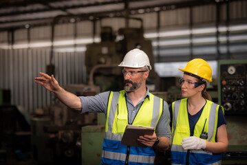 Caucasian male engineer holding tablet and female assistance in safety uniforms Inspection and maintenance planning the machinery in heavy industrial manufacturer factory.