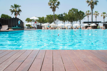 Wooden deck in front with blurred background of swimming pool in hotel