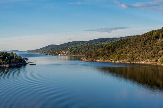 stilles glattes Wasser des Fjords im Vordergrund mit hügelig bewaldeter Landschaft im Hintergrund © URS.INHO