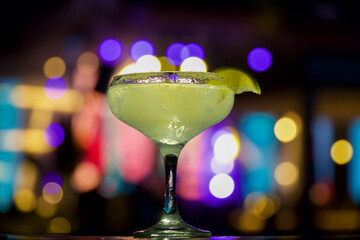 Cocktail in the bar. Cocktail margarita with a slice of lemon close up, on the background of the colorful night lights of the club
