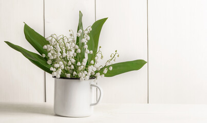Bouquet of tender lilies of the valley in an iron mug. Wooden white background.