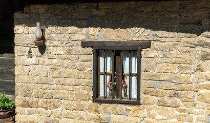 wall of a stone house with a wooden window and an old lamp