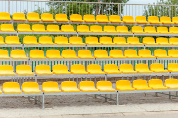 Empty vacant stadium stands, chairs, plastic yellow arena spectator seats on a small football...