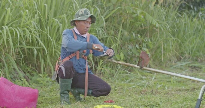 Asian male farmer tanned skin wearing a blue shirt, Change the blade used to cut the grass.
