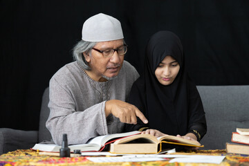 muslim father teaching his daughter about practicing reading textbook on black background