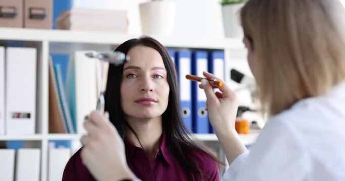 Female doctor checking woman patien eyes with flashlight in medical office