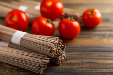 Buckwheat pasta with cherry tomatoes on brown wood. Raw pasta. Ingredients for a gluten free dish. Healthy food. Place to copy.