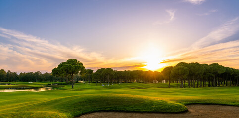 Golf course at sunset with beautiful sky and sand trap. Scenic panoramic view of golf fairway with...