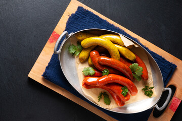 Food concept Assortment european homemade organic spicy sausage in aliminum tray on wooden board with black slate stone board with copy space