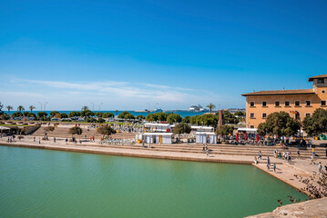 Fototapeta na wymiar Mallorca, Spain. April 27, 2022. Tourists exploring at sea promenade in city. Male and female travelers enjoying vacation in historic town. Scenic view of seaside by buildings against blue sky.