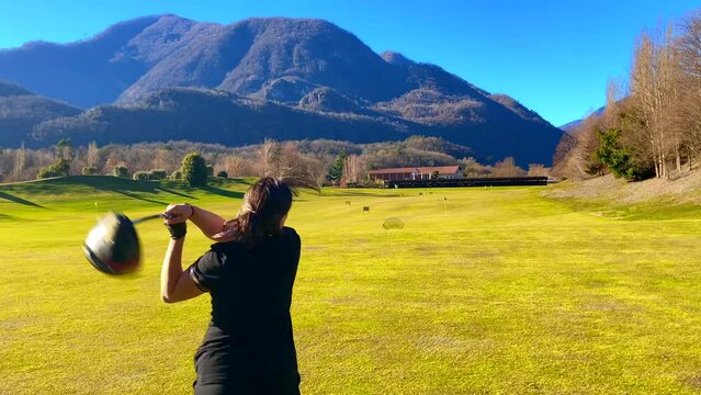 Golfer Training with Her Golf Club Driver in Driving Range with Mountain View in a Sunny Day in Losone, Ticino, Switzerland.